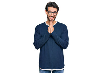 Young hispanic man wearing casual clothes and glasses praying with hands together asking for forgiveness smiling confident.