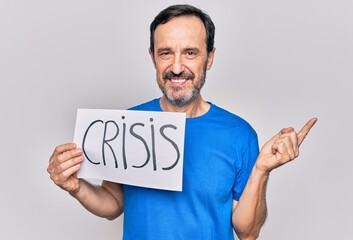 Middle age handsome man holding paper with crisis message over isolated white background smiling happy pointing with hand and finger to the side