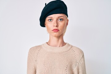 Young blonde woman wearing french look with beret with serious expression on face. simple and natural looking at the camera.