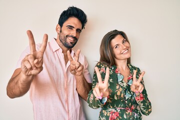Beautiful young couple of boyfriend and girlfriend together smiling looking to the camera showing fingers doing victory sign. number two.