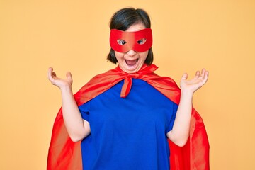 Brunette woman with down syndrome wearing super hero costume celebrating victory with happy smile and winner expression with raised hands