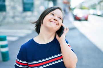 Beautiful brunette woman with down syndrome at the town on a sunny day talking on smartphone