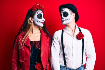 Couple wearing day of the dead costume over red smiling looking to the side and staring away thinking.
