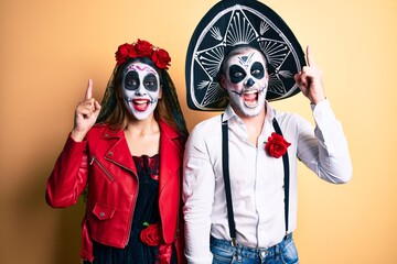 Fototapeta na wymiar Couple wearing day of the dead costume over yellow pointing finger up with successful idea. exited and happy. number one.