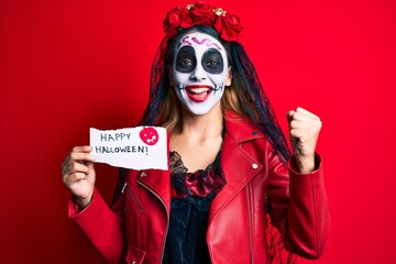 Woman wearing day of the dead costume holding happy halloween paper screaming proud, celebrating victory and success very excited with raised arms