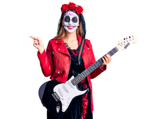 Woman wearing day of the dead costume playing electric guitar smiling happy pointing with hand and finger to the side