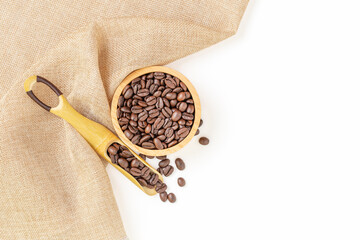Coffee beans roasted in a wooden bowl and beans scoop on sackcloth over white background. Top view.