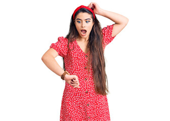 Brunette teenager girl wearing summer dress looking at the watch time worried, afraid of getting late