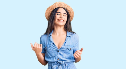 Brunette teenager girl wearing summer hat very happy and excited doing winner gesture with arms raised, smiling and screaming for success. celebration concept.
