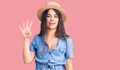 Brunette teenager girl wearing summer hat showing and pointing up with fingers number four while smiling confident and happy.