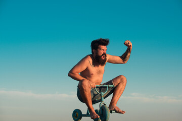 Guy riding childs tricycle. Portrait of a bearded man as a crazy hipster having fun with bicycle...