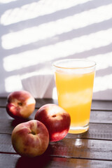 peaches on white wood with American blind light with glass juice glass and a knife next to it