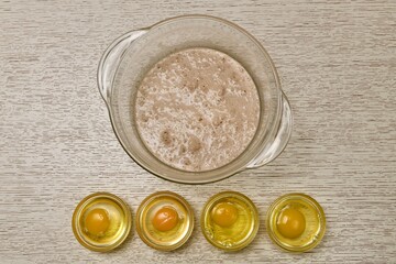  The stage of preparing eggs for kneading yeast dough. Deep glass bowl with yeast in milk. Four raw eggs in a bowl.