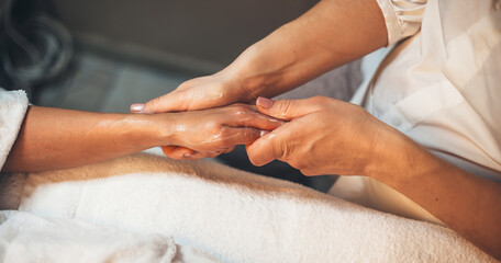 Fototapeta na wymiar Caucasian spa worker massaging client's hand with special lotion during a hand massage session at spa salon