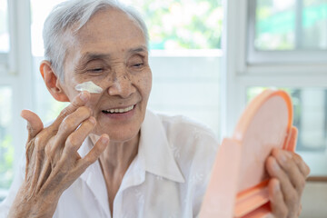 Happy smiling asian senior woman apply sunscreen lotion on the cheek,protect her beautiful face,old...