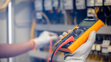 Electrician engineer uses a multimeter to test the electrical installation and power line current in an electrical system control cabinet. - obrazy, fototapety, plakaty