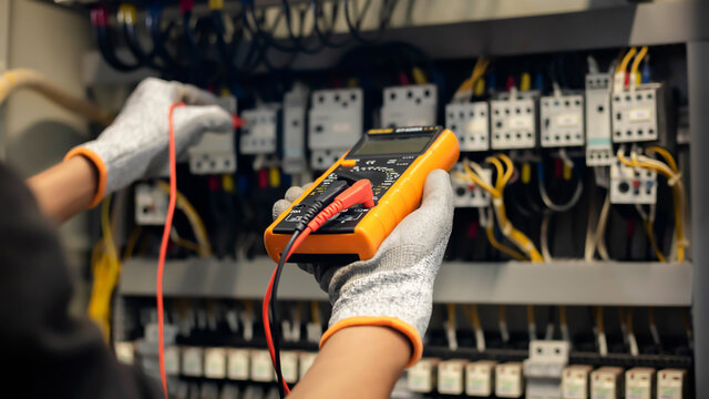 Electrician engineer uses a multimeter to test the electrical installation and power line current in an electrical system control cabinet.