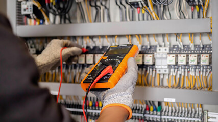 Electrician engineer uses a multimeter to test the electrical installation and power line current in an electrical system control cabinet.