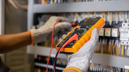 Electrician engineer uses a multimeter to test the electrical installation and power line current in an electrical system control cabinet.