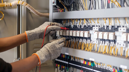 Electrician engineer uses a multimeter to test the electrical installation and power line current in an electrical system control cabinet.