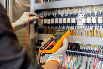 Fototapeta na wymiar Electrician engineer uses a multimeter to test the electrical installation and power line current in an electrical system control cabinet.