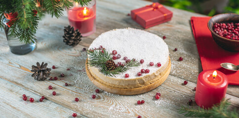 Festive white mousse cake covered with coconut flakes imitating snow and decorated with red berries, cones and fir branches. Concept of the New year and Christmas