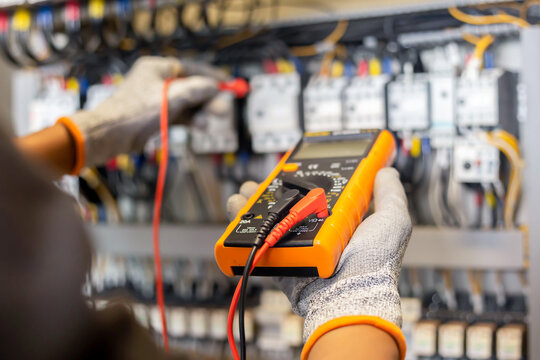 Electrician engineer uses a multimeter to test the electrical installation and power line current in an electrical system control cabinet.