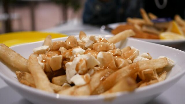 Closeup of a Poutine dish at a restaurant. The poutine is a Quebec meal made from french fries, gravy and cheese.
