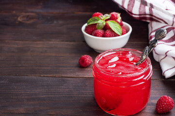 Homemade raspberry jam in a glass jar and fresh raspberries with mint on a wooden rustic background. Copy space