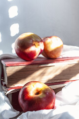 peaches under window light on red books with a white cloth and a knife on white cloth and white background