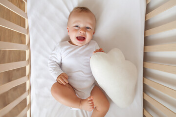 Funny blond cute baby lying and laughing in white children bed