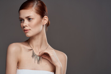 Fototapeta premium Beautiful woman decorating naked shoulders cosmetics collected hair in a bun gray background
