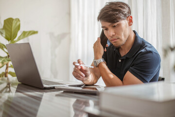 Man working on laptop and talking with smartphone.