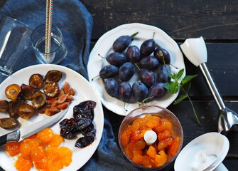 Blue ripe plum on a dark background with a blue napkin. The process of making cream juice from natural plums or smoothie using a mixer. View from above.