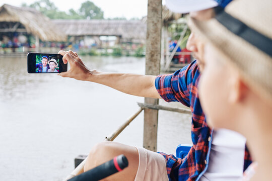 Mature Vietnamese man taking selfie with son when they are fishing on weekend