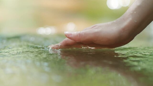 Hand touching water in the green forest river or lake. Travel enjoying feel the nature and life concept in slow motion.