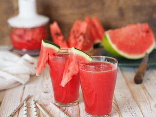 Glasses of fresh juice, watermelon smoothie on the table in the kitchen.Ripe watermelons and slices in the background. Healthy natural food. Watermelon is a popular organic food product.