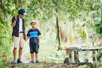 Happy father walking to river with son to show him how to catch fish