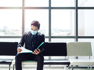 Asian businessman in suit wearing protective face mask sitting and review his resume and waiting...