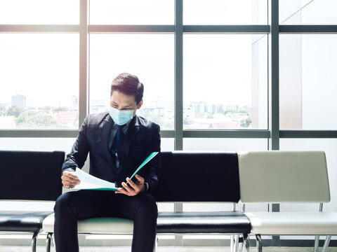 Asian Businessman In Suit Wearing Protective Face Mask Sitting And Review His Resume And Waiting For Job Interview.