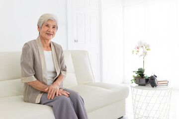 smart old asian female sitting on sofa, she feeling happy and smile, happiness retirement