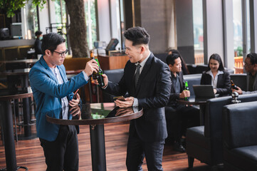 Businessmen and women are smiling and clanging glasses of alcoholic of beer and beverage together after work