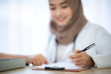 The muslim woman doctor record and note diagnostic result exam and medical history of the patient file to document report on the computer laptop