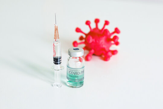 Syringe with vaccine injection next to a red corona virus on the white background. Theme of health care, medical treatment and disease prevention