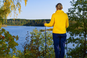 hiking concept, outdoor lifestyle. Woman in yellow sweater and Trekking pole looking at the lake after hike on a sunny day.