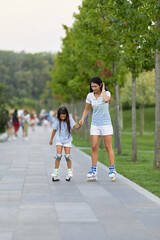 Young mother and her little daughter rollerskating in park. happy family