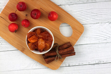 bowl of apple jam, red apples and cinnamon sticks on cutting board on white wooden background flat lay