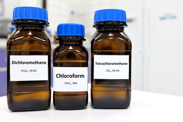 Selective focus of pure dichloromethane, chloroform and tetrachloromethane liquid chemical compound set in dark glass bottles inside a chemistry laboratory with copy space. Set of industrial solvents.