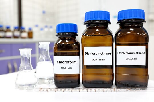 Selective focus of pure dichloromethane, chloroform and tetrachloromethane liquid chemical compound set in dark glass bottles inside a chemistry laboratory with copy space. Set of industrial solvents.