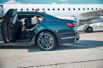 Smiling mature businessman in car near plane
